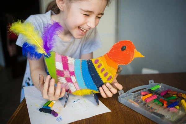 Řemeslo s dětmi. jasný pták, vystřižený z lepenky a malovaný voskovými pastelkami, v rukou dítěte. proces vytváření — Stock fotografie