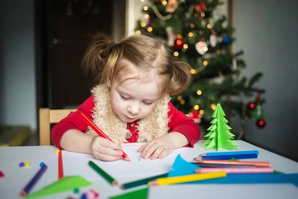 Çocuk Noel Baba 'ya bir mektup yazıyor. Küçük bir kız Noel ağacının arka planına pastel boyalarla resim çiziyor. Çocuklar için yeni yıl yaratıcılığı kavramı