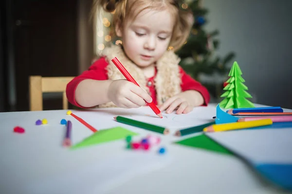 아이는 산타클로스에게 편지를 쓴다. 크리스마스 트리의 배경에서 어린 소녀가 크레용으로 그림을 그립니다. 새해가 되면 아이들의 창의력이라는 개념은 — 스톡 사진