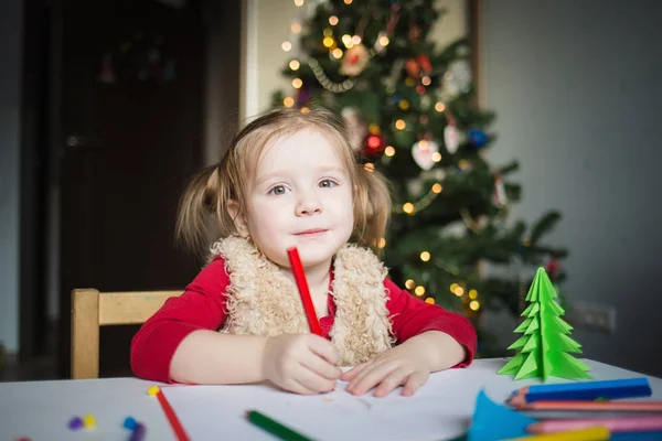 Çocuk Noel Baba 'ya bir mektup yazıyor. Küçük bir kız Noel ağacının arka planına pastel boyalarla resim çiziyor. Çocuklar için yeni yıl yaratıcılığı kavramı