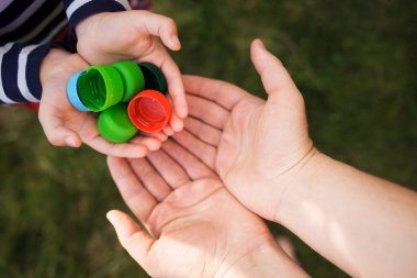Bebek, annesinin ellerine plastik kapaklar koyuyor. Ebeveyni ve çocuğu siper alıyor. Geri dönüştürülebilir. şişe kapağı koleksiyonu.