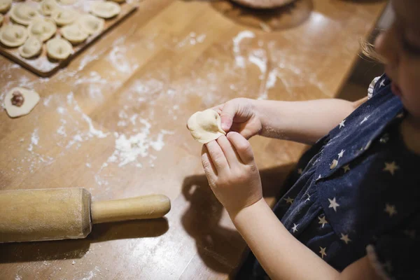 Küçük çocuk evde, mutfakta, masada hamur tatlısı yapıyor. Çocuklarla yemek pişirmek. Oyunda ince motor becerilerin geliştirilmesi.