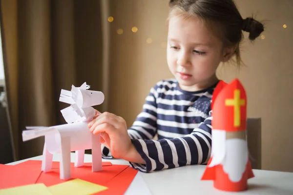 Çocuklar için kağıt işi. Aziz Niklas ve beyaz at sinterklaas günü için oyuncak. Çocuklar için sanat yaratmak. Kız atı yapıştırıyor..