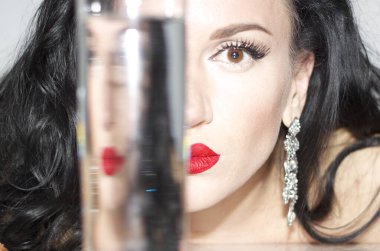 Profesyonel makyajlı güzel bir kadın. Bir bardak suya yansıyan altın tırnaklar.