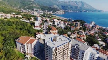 Budva bir kuş bakışı ile. Becici. Dron bir yükseklikten fotoğraf çeker. Deniz, gökyüzü, objektif eski tarzda ev sahipliği yapmaktadır. Kahverengi çatılar tatil beldesi. Modern otel deniz kenarında. Bağlantı noktası ile demirli yatlar.