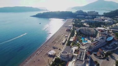 Budva bir kuş bakışı ile. Becici. Dron bir yükseklikten fotoğraf çeker. Deniz, gökyüzü, objektif eski tarzda ev sahipliği yapmaktadır. Kahverengi çatılar tatil beldesi. Modern otel deniz kenarında. Bağlantı noktası ile demirli yatlar.