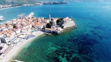 Budva bir kuş bakışı ile. Becici. Dron bir yükseklikten fotoğraf çeker. Deniz, gökyüzü, objektif eski tarzda ev sahipliği yapmaktadır. Kahverengi çatılar tatil beldesi. Modern otel deniz kenarında. Bağlantı noktası ile demirli yatlar.