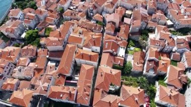Budva bir kuş bakışı ile. Becici. Dron bir yükseklikten fotoğraf çeker. Deniz, gökyüzü, objektif eski tarzda ev sahipliği yapmaktadır. Kahverengi çatılar tatil beldesi. Modern otel deniz kenarında. Bağlantı noktası ile demirli yatlar.