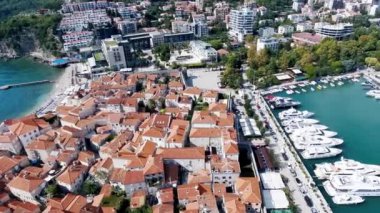 Budva bir kuş bakışı ile. Becici. Dron bir yükseklikten fotoğraf çeker. Deniz, gökyüzü, objektif eski tarzda ev sahipliği yapmaktadır. Kahverengi çatılar tatil beldesi. Modern otel deniz kenarında. Bağlantı noktası ile demirli yatlar.