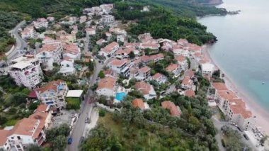 Budva bir kuş bakışı ile. Becici. Dron bir yükseklikten fotoğraf çeker. Deniz, gökyüzü, objektif eski tarzda ev sahipliği yapmaktadır. Kahverengi çatılar tatil beldesi. Modern otel deniz kenarında. Bağlantı noktası ile demirli yatlar.