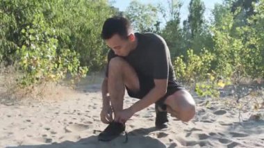 Ayakkabı bağcıklarını bağladıktan sonra atlet. Kumda bir çalışmadan sonra eğitim genç bir adam.