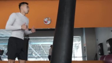 Genç bir Asyalı kickboks spor salonunda eğitim alıyor. Atlet kum torbasına tekme atıyor. Aynalı spor salonu.