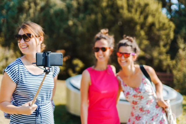 三个年轻女性游客穿着夏装 在阳光明媚的秋日里 用自拍棒和手机自画像 — 图库照片