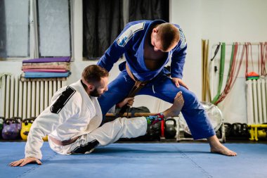 Brezilyalı Jiu Jitsu BJJ dövüş sanatları eğitimi akademide idman yapıyor iki dövüşçü de la riva muhafız pozisyonu almış kahverengi kemerli bir kimonoyla tatbikat teknikleri uyguluyorlar.