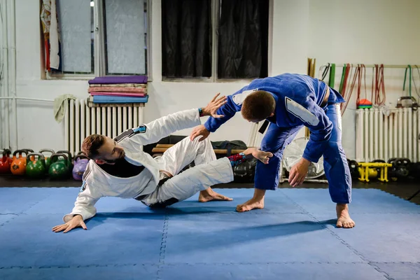 Brezilyalı Jiu Jitsu BJJ dövüş sanatları eğitimi akademide antrenman yapıyor. Teknik olarak iki dövüşçü savunma pozisyonu alıyor. Gi kimono savunma talimi teknikleri uyguluyorlar.