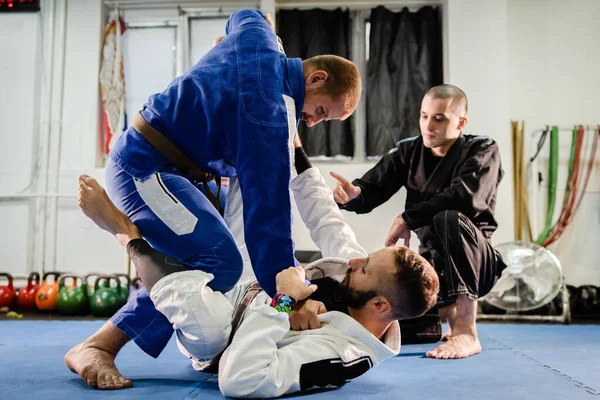 Brazilian JIu Jitsu BJJ private class professor of the martial arts academy working on the technique details with his students black and brown belts training open guard in kimono gi