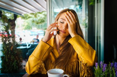 Kafe restoranında cep telefonuyla konuşan genç ve güzel bir kadının portresi. Alnıyla başını tutarak rahatsız edici bir sürpriz haber alıyor.