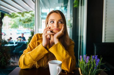 Kafe restoranında cep telefonuyla konuşan genç ve güzel bir kadının portresi. Sıkıcı bir konuşma.