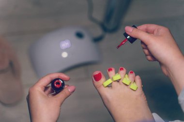 Ayak parmaklarına jöle sürerken yandan görüş evde pedikür yapan kimliği belirsiz bir kadın ayak tırnaklarına jöle sürerken üst görünüm koyu renk oda güzelliği konsepti.
