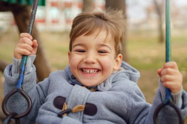 Üç yaşında beyaz bir çocuğun portresi. Kışın veya sonbaharda parkta salıncakta palto giyerek eğleniyor.