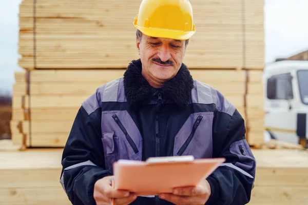 Portrait of caucasian senior man construction worker general laborer building contractor wearing yellow protective helmet holding pen and document checking data report project on the site