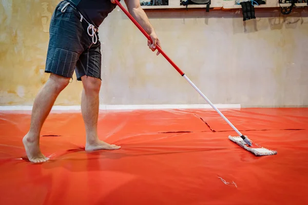 Unknown caucasian man cleaning tatami mats at MMA or BJJ or Judo wrestling martial arts gym using mop to swipe and disinfect due to coronavirus pandemic or bacteria fungus preventing infection