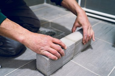 İnşaat işçisi duş seramik fayans su bariyeri için banyoya beton tuğla örüyor.