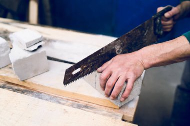 Tuğla yalıtım malzemesi beton taşını elle kesmek için el testeresini kullanan inşaat işçisine yaklaş.