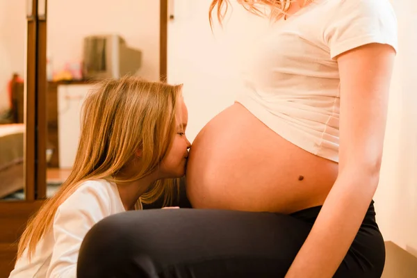 小女孩站在家里 吻着妈妈怀孕的肚子 等着孩子 — 图库照片