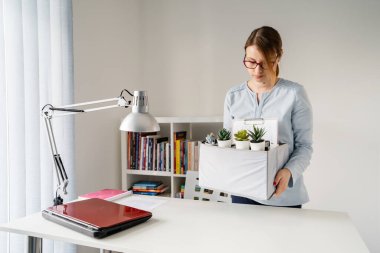 İşten kovulduktan sonra iş yerindeki masanın başında duran beyaz kadın hakkında ön görüş. Kriz nedeniyle işten çıkarılan kişisel eşyalarını kutuya koyuyor.