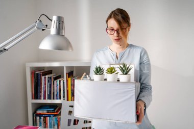 İşten kovulduktan sonra iş yerindeki masanın başında duran beyaz kadın hakkında ön görüş. Kriz nedeniyle işten çıkarılan kişisel eşyalarını kutuya koyuyor.