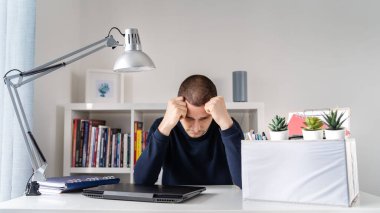 Masanın başında oturan beyaz yetişkin bilgisayarının başında duruyor. Ekonomik kriz nedeniyle işten kovulduktan sonra kişisel eşyalarıyla dolu kutusunu işten çıkarttırıyor.