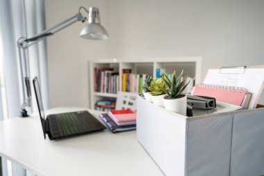 Kişisel eşyalarla dolu bir kutu ofisteki beyaz masaya ya da eve dizüstü bilgisayarın yanına yerleştirilmiş kovulduktan sonra taşınmaya hazır ya da iş yerinde işe alınmaya hazır.