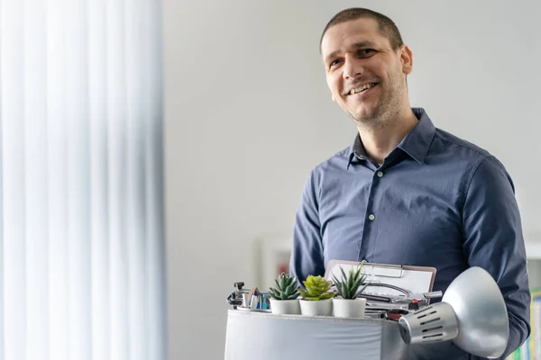 Portrait of caucasian man smiling holding the box with his personal stuff at office - Male adult happy after quitting the job at company - Young worker taking his personal belongings to new workplace