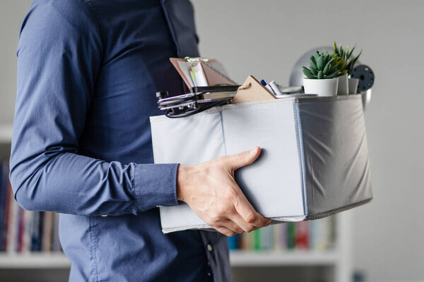 Midsection close up of unknown caucasian man holding a box with personal items stuff leaving the office after being fired from work due recession economic crisis downturn losing job company shutdown