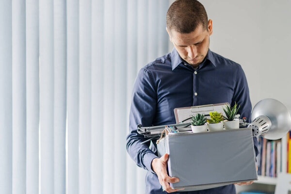 Portrait of adult caucasian man businessman wearing shirt holding a box personal items stuff leaving the office being fired from work due recession economic crisis downturn losing job company shutdown