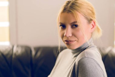 Sarışın güzel bir kadının portresi. Evdeki yatağın üzerinde oturan kameraya bakıyor.