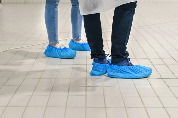 Bilinmeyen kadın ve erkeğin ayakkabılarına yakından bakın - hastanenin zemininde korunmak için mavi tıbbi ayakkabı kılıfı - terlikler için tıbbi antibakteriyel plastik çekiş standart terlik