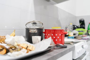 Kirli tencerelerle beyaz mutfağa yan bakış ve mutfak aletleri mutfak malzemeleriyle dolu mutfak tezgahları dağınık.