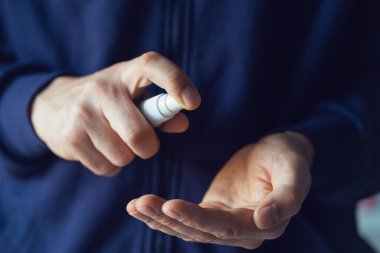 Ön taraf, kimliği belirsiz erkek, beyaz adam sprey ile dezenfekte edilen alkol ürününü uyguluyor. Evde ya da işte virüslü bakteri sağlığını önlemek için elleri dezenfekte ediyor.
