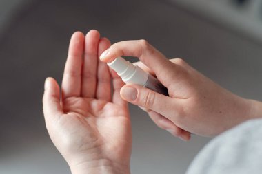 Kimliği belirsiz beyaz kadın ya da kız çocuğuna yüksek açılı bakış açısı sprey dezenfeksiyon alkollü ürün uyguluyor ellerde dezenfekte oluyor evde ya da işte virüslü bakterilerin sağlığını önlüyor.