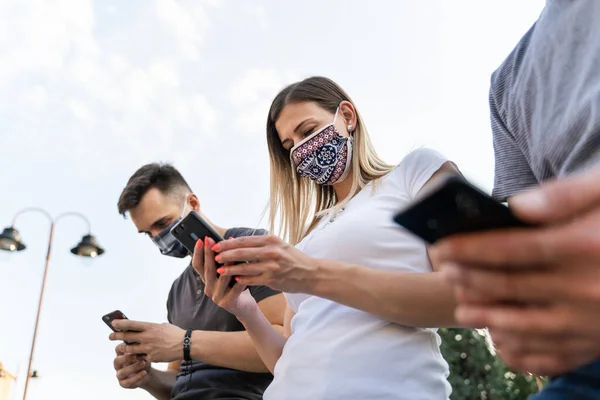 使用手机的高加索男人和女人的低视角 现代通信在线发短信社交网络信息 戴面具的男人和女人拿着手机 社交距离新常态概念 — 图库照片