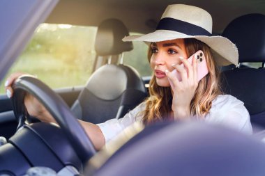 Araba kullanırken cep telefonu kullanan genç ve güzel bir kadın, beyaz bir kadın, elinde direksiyonla arabasında telefonla konuşuyor.