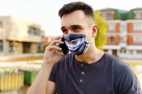 头戴防护面罩的年轻的高加索男子 在隔离关闭后的第二天在城市里用手机交谈的男性成年人 在大流行病中出现的新的正常概念 — 图库照片