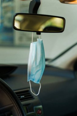Dikiz aynasındaki arabadaki tıbbi koruyucu yüz maskesi - Aracın dikiz aynasındaki Covid-19 pandemik koruma - koronavirüs salgını yeni normal önleme kavramı