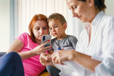 Anne ve oğul evdeki sosyal medyayı inceliyor - Kafkas kadın ve oğlu cep telefonu kullanarak fotoğrafları yüklüyor ve internete mesaj yolluyorlar - gerçek insanlar boş zaman aktivitesi ev hayatı kavramı