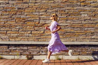 Yazın güneşli bir günde, taş duvarın önünde mor elbiseler içinde koşan olgun, beyaz kadın, özgürlük ve neşe kavramını terk ediyor.