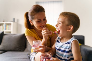 Anne ve yakında evde beslenen beyaz bir kadın kanepeye oturmuş küçük bir çocuğu çöl ile besliyor - yakın plan - ev hayatı neşesi ve çocukluk kavramını bağlayan gerçek insanlar