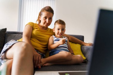 Küçük beyaz çocuk ekranı işaret ediyor ve bilgisayardan annesini gösteriyor - küçük çocuk annesinin yanında oturuyor - çocukluk konsepti