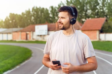 Akıllı telefon ve kulaklıklarla koşu pistinde duran bir adam - Yetişkin beyaz erkek eğitim istatistiklerini izlemek için mobil uygulama kullanıyor - bir çağrı mesajı gönderiyor - gerçek insanlar konsepte odaklanıyor